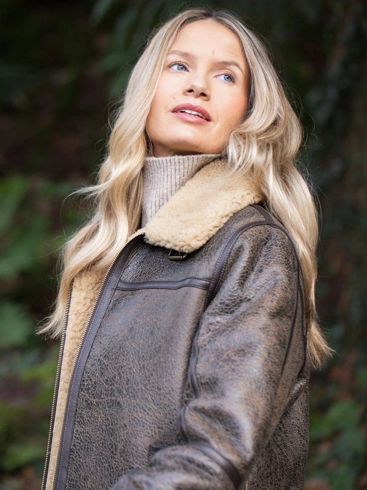 Woman wearing a brown Cawfell Shearling Aviator Jacket with fur lining, standing outdoors.