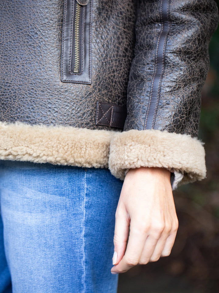 Close-up of a person wearing a Cawfell Shearling Aviator Jacket with shearling trim and blue jeans.