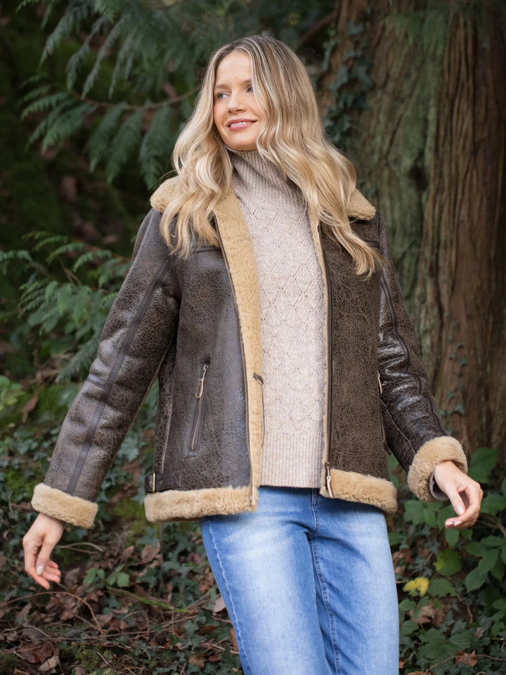 Woman wearing a brown shearling Cawfell Shearling Aviator Jacket with beige trim outdoors.