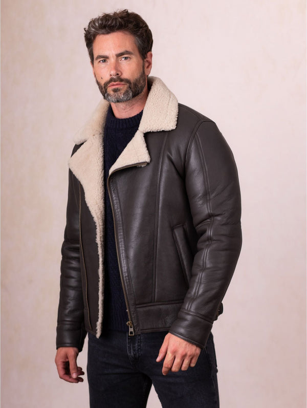 Man wearing a Javelin Sheepskin Aviator Jacket leather jacket with white fur lining against a beige background